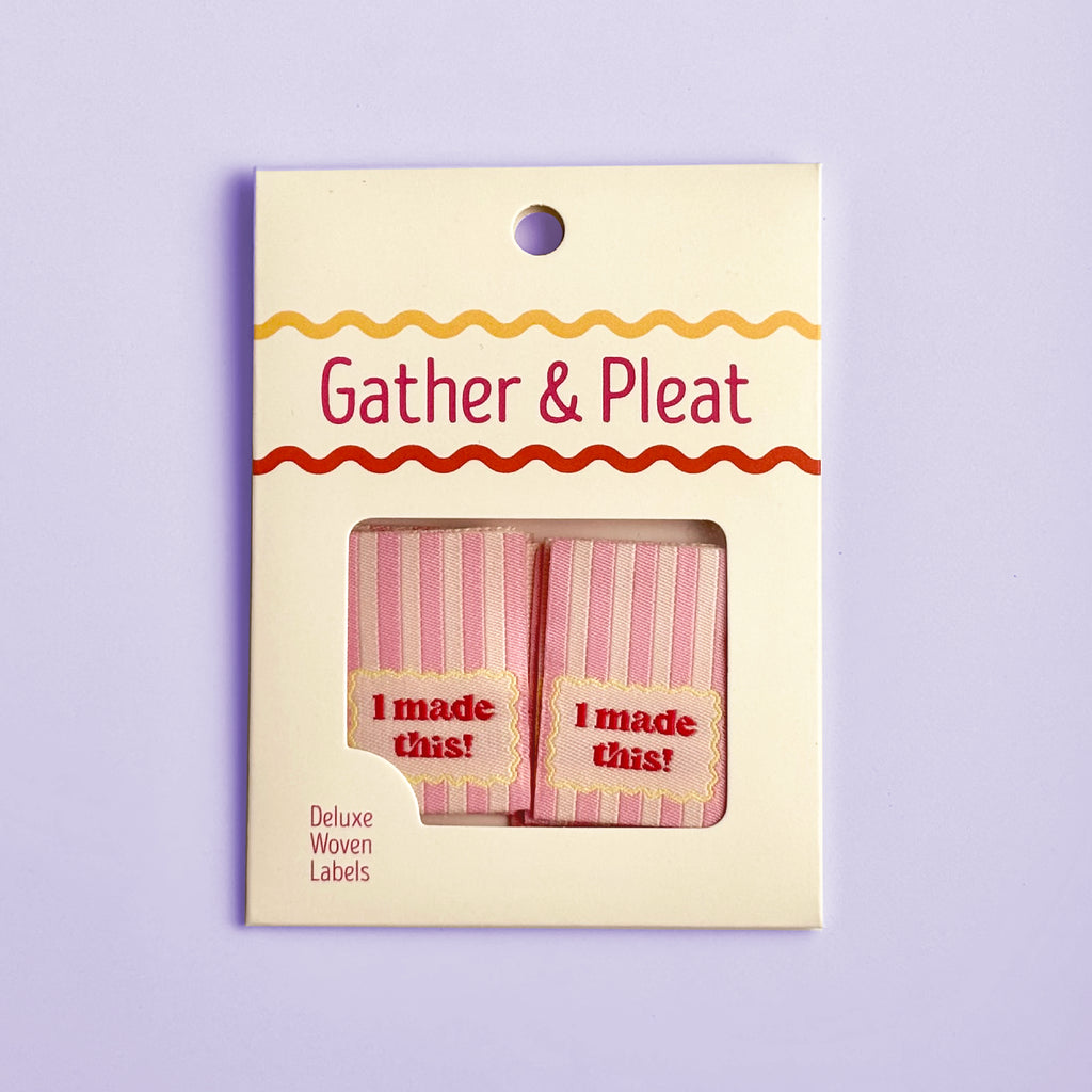 Pack of six 'I Made This!' woven sewing labels in Gather & Pleat retail packaging, on a lilac background.